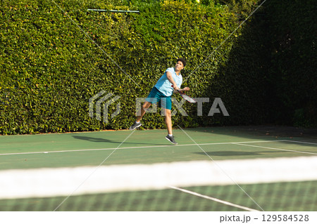 Asian man leaping into air swinging tennis racket near net on tennis court wearing sportswear Asian man leaping into air swinging tennis racket near net on tennis court wearing sportswear 129584528