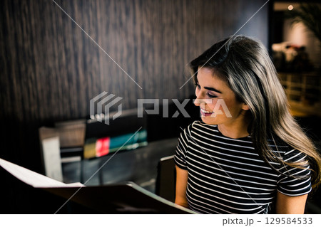 Woman holding menu, reading it while sitting at restaurant table with wooden slat wall, copy space 129584533