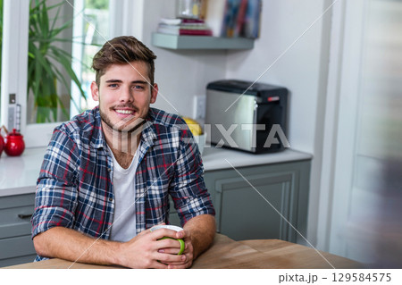 Man sitting at kitchen table holding ceramic mug near toaster and fruit bowl gazing at window Man sitting at kitchen table holding ceramic mug near toaster and fruit bowl gazing at window 129584575