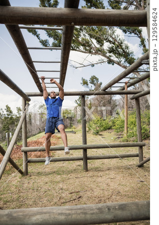 Mid adult man in blue athletic shirt hanging from wooden monkey bars at outdoor fitness course 129584624