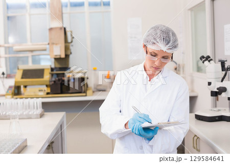Female scientist wearing lab coat writing on clipboard at bench with test tube rack, copy space 129584641