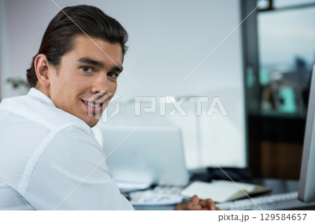 Man in his 30s turning head and torso at office desk with computer monitor, copy space 129584657