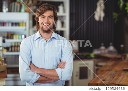 Bearded man standing with arms crossed in cafe with wooden service counter and glass cake domes Bearded man standing with arms crossed in cafe with wooden service counter and glass cake domes 129584686
