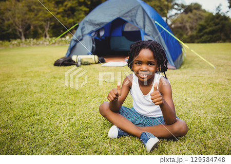 African American boy sitting cross-legged on green lawn beside gray tent with sleeping pad and bag African American boy sitting cross-legged on green lawn beside gray tent with sleeping pad and bag 129584748