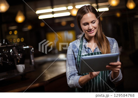 Woman wearing striped apron tapping tablet behind counter at cafe with espresso machine, copy space Woman wearing striped apron tapping tablet behind counter at cafe with espresso machine, copy space 129584768