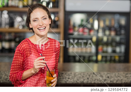 Female patron standing at bar counter holding glass of drink near refrigerated display, copy space 129584772