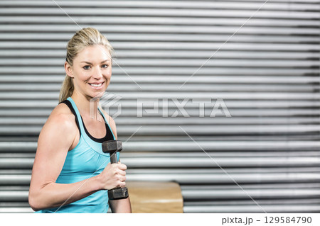 Woman in thirties lifting hexagonal dumbbell at gym beside wooden box in turquoise top, copy space 129584790