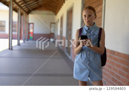 Girl student standing in school corridor holding smartphone and backpack, copy space Girl student standing in school corridor holding smartphone and backpack, copy space 129584803