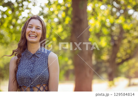 Teenage girl standing in sunlit park wearing blue floral top with lace-up waist cutouts, copy space 129584814