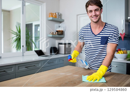 Man wearing yellow rubber gloves cleaning countertop with spray bottle near laptop, copy space 129584860