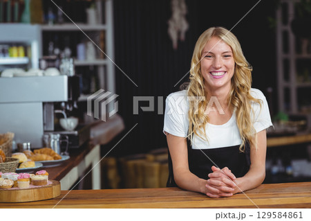 Woman barista standing behind wooden countertop in cafe, serving cupcakes and espresso, copy space 129584861