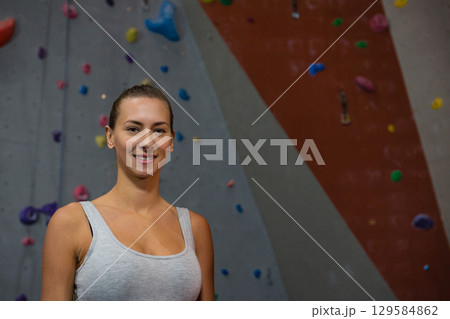 Woman standing and smiling in climbing gym in tank top near colorful climbing holds, copy space 129584862