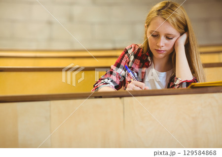 Teen female student writing in notebook with blue pen in classroom wearing plaid shirt, copy space 129584868