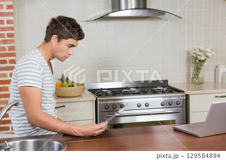 Man standing at home kitchen island using utensils and checking laptop near fruit bowl, copy space Man standing at home kitchen island using utensils and checking laptop near fruit bowl, copy space 129584894