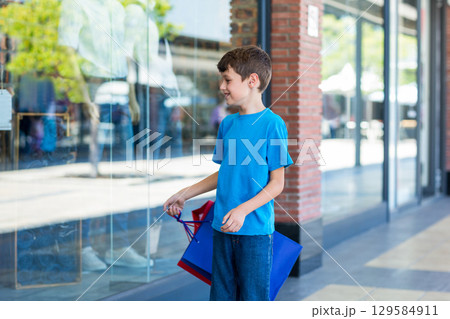 Boy standing outside retail store holding shopping bags, gazing at mannequins, copy space Boy standing outside retail store holding shopping bags, gazing at mannequins, copy space 129584911