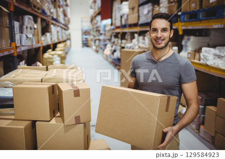 Male warehouse worker holding cardboard box standing in aisle with metal shelving, copy space Male warehouse worker holding cardboard box standing in aisle with metal shelving, copy space 129584923