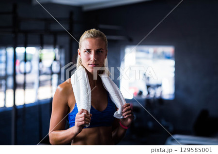 Woman wearing blue sports bra standing near pull-up bars in gym holding towel and fitness tracker Woman wearing blue sports bra standing near pull-up bars in gym holding towel and fitness tracker 129585001