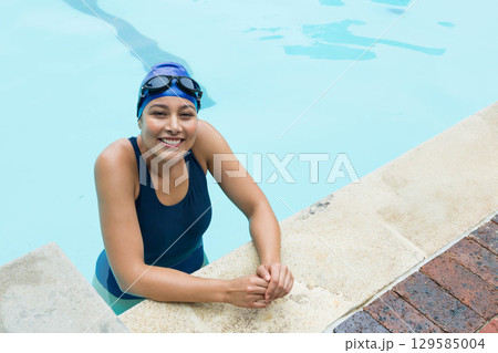 Female swimmer emerging at outdoor pool, gripping edge and wearing swimsuit and goggles, copy space Female swimmer emerging at outdoor pool, gripping edge and wearing swimsuit and goggles, copy space 129585004