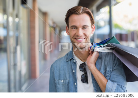 Man in late twenties standing in mall corridor holding paper shopping bags and sporting sunglasses Man in late twenties standing in mall corridor holding paper shopping bags and sporting sunglasses 129585006