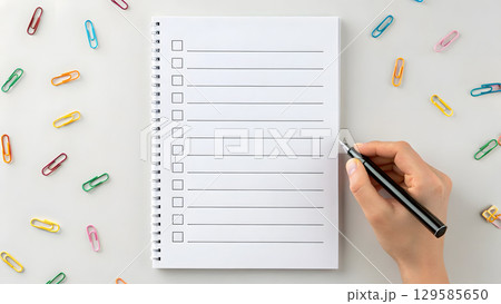 Creating a checklist on a notebook with colorful clips scattered around the desk 129585650