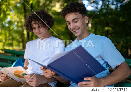 Two teens in the park preparing for the lessons and reading a book Two teens in the park preparing for the lessons and reading a book 129585711