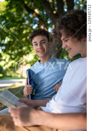Two teens in the park preparing for the lessons and reading a book Two teens in the park preparing for the lessons and reading a book 129585712