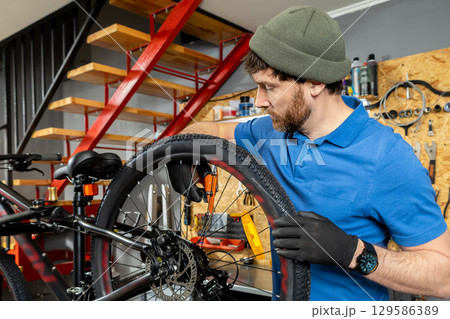 Mechanic in blue shirt adjusting bicycle rear wheel with precision in indoor garage Mechanic in blue shirt adjusting bicycle rear wheel with precision in indoor garage 129586389