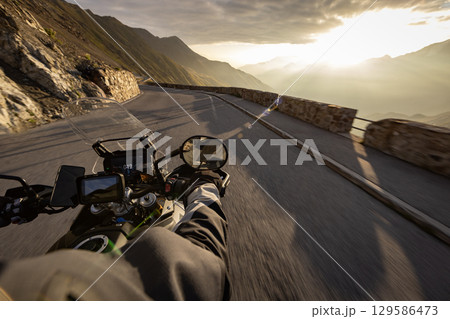 Motorcycle rider riding in Italian Alps during sunrise , handlebar view , dramatic sky . Travel and freedom, outdoor activities 129586473