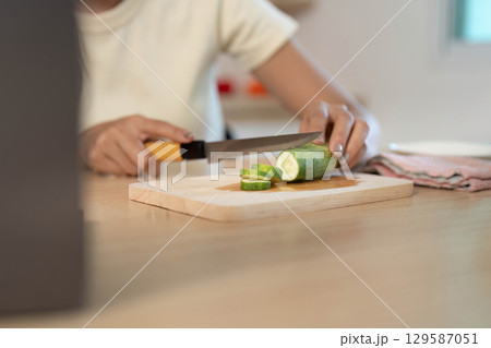 Healthy Cooking. Woman slicing cucumber in a bright kitchen. Healthy Cooking. Woman slicing cucumber in a bright kitchen. 129587051