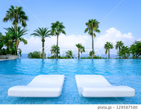 Luxurious Infinity Pool with pair loungers surrounded by palms and ocean view 129587580