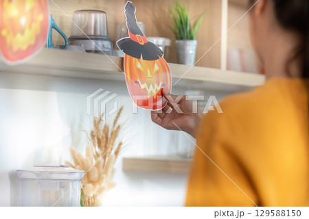 Halloween Decor. Woman placing a pumpkin decoration on a shelf for festive spirit. 129588150