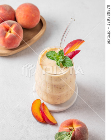 Smoothie with peach and banana in a glass on a light background with tropical fruits. 129588879
