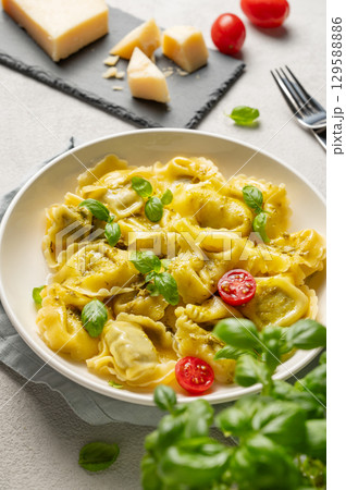 Tortellini pasta with parmesan, pesto and basil in a plate on a light background with tomato Tortellini pasta with parmesan, pesto and basil in a plate on a light background with tomato 129588886