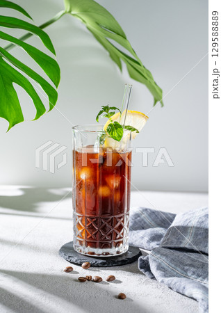 Cold brew coffee tonic in a glass with lemon and ice on a light background with coffee beans Cold brew coffee tonic in a glass with lemon and ice on a light background with coffee beans 129588889