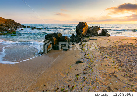 landscape by the sea at sunrise in summer. beautiful beach with rocks washed by calm waves in orange light. view to horizon under blue sky with clouds. scenic travel destination for leisure and relax 129589965