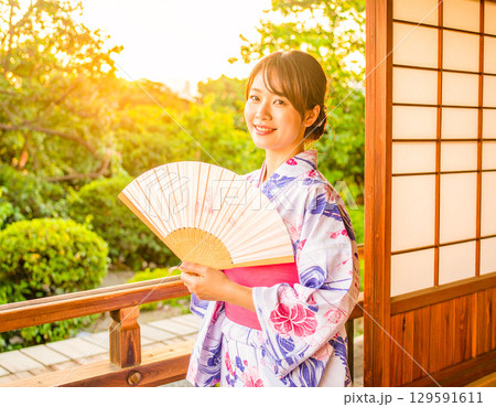 夏の夕暮れの縁側と庭園に佇む浴衣姿の女性 129591611