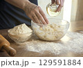 Close-up of female hands adding oil to the dough, on the background of flour and a rolling pin, the concept of home baking. 129591884