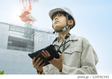工事現場でタブレットを見る作業服の若いビジネスマン 129592391