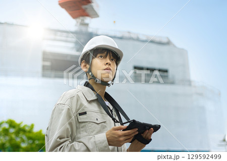工事現場でタブレットを見る作業服の若いビジネスマン 129592499