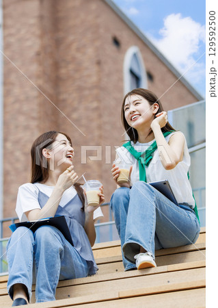 友達とキャンパスの階段ベンチに座る大学生 友達とキャンパスの階段ベンチに座る大学生 129592500