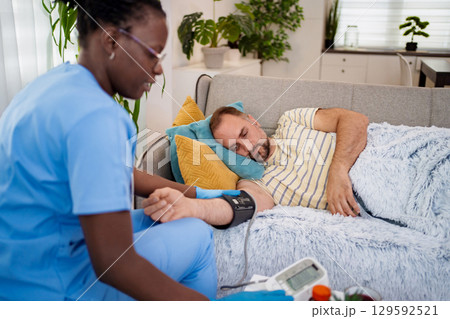Caring nurse checks blood pressure of patient at home 129592521