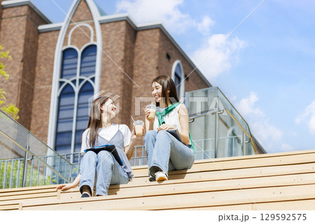 友達とキャンパスの階段ベンチに座る大学生 129592575