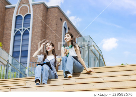 友達とキャンパスの階段ベンチに座る大学生 129592576