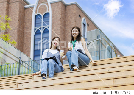 友達とキャンパスの階段ベンチに座る大学生 129592577