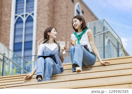 友達とキャンパスの階段ベンチに座る大学生 129592585
