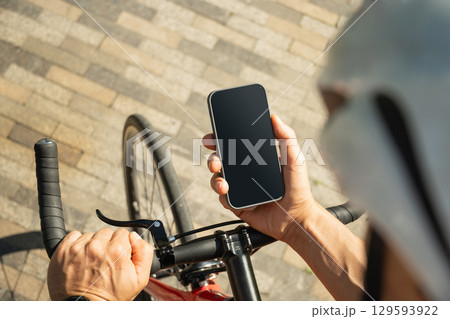 Male cyclist in helmet with mobile phone on bike check apps at park. Space for design. View from above. Close up. Male cyclist in helmet with mobile phone on bike check apps at park. Space for design. View from above. Close up. 129593922
