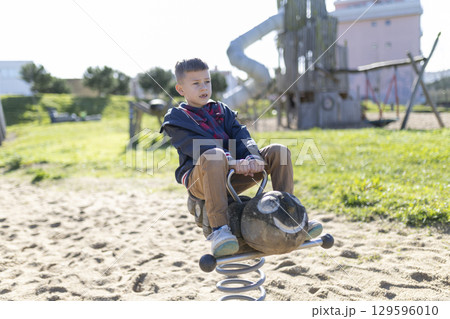 Child playing on spring rider at playground on sunny day Child playing on spring rider at playground on sunny day 129596010