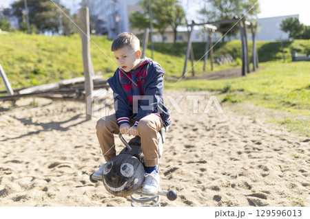 Child playing on a wooden rocking horse in a playground 129596013