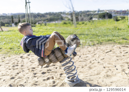 Child playing on spring rider in playground on sunny day 129596014