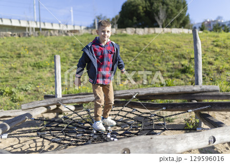 Young boy balancing on rope net at playground in sunny day 129596016